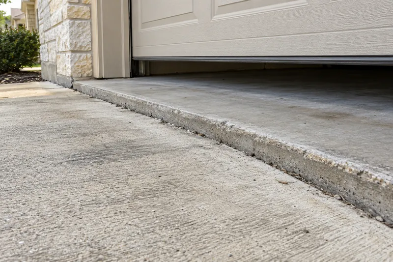 A driveway panel sunk at the garage door, leaving a raised trip edge