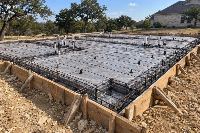 A formed house slab with plumbing stubs and a plastic vapour barrier, before the pour