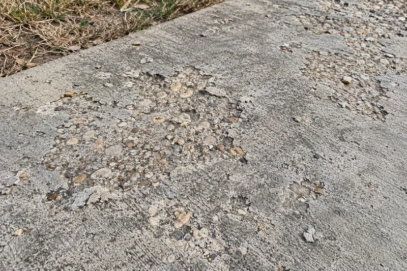 Scaled concrete surface flaking off to show the stone underneath